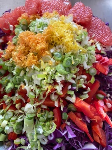 A bowl of shredded red cabbage, sliced red pepper and scallions, topped with grated zest and ruby grapefruit segments.